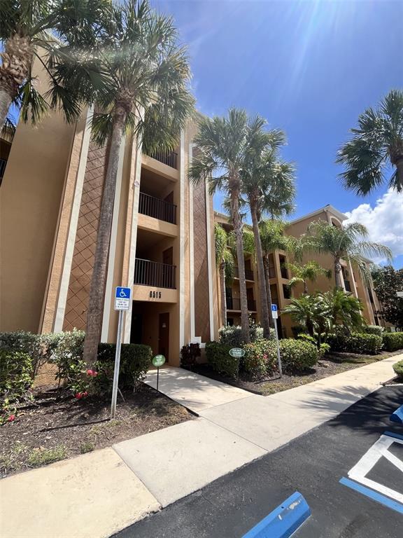 A multi-story apartment building exterior features tan stucco walls, balconies, and surrounding palm trees — 6515 GRAND ESTUARY TRAIL UNIT 403, BRADENTON, FL