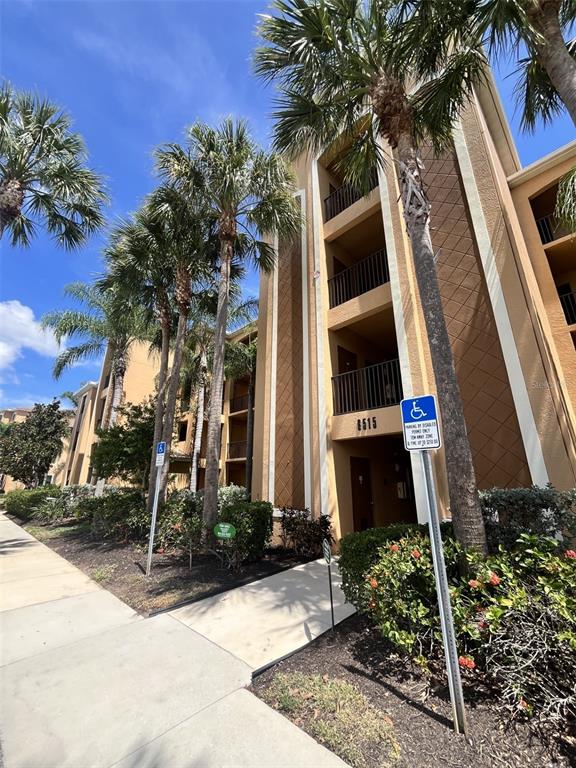 A multi-story tan apartment building features palm trees and a handicap parking sign — 6515 GRAND ESTUARY TRAIL UNIT 403, BRADENTON, FL