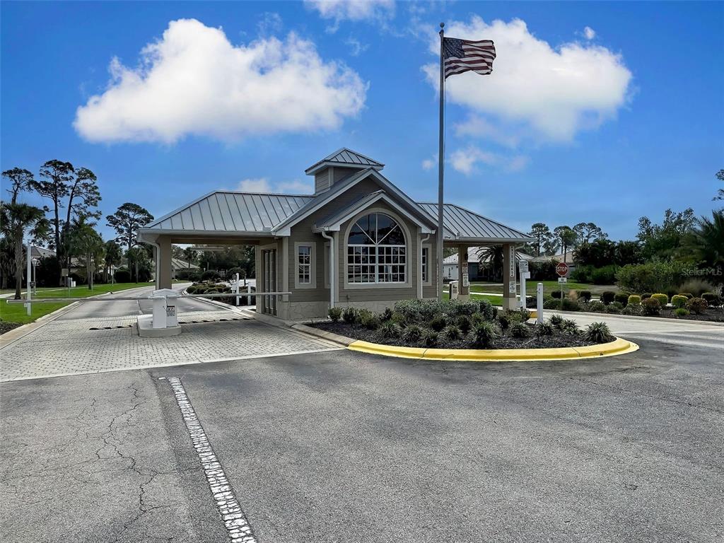 A gated community entrance features a guardhouse with a metal roof and an American flag — 1645 PALMETTO PALM WAY, NORTH PORT, FL