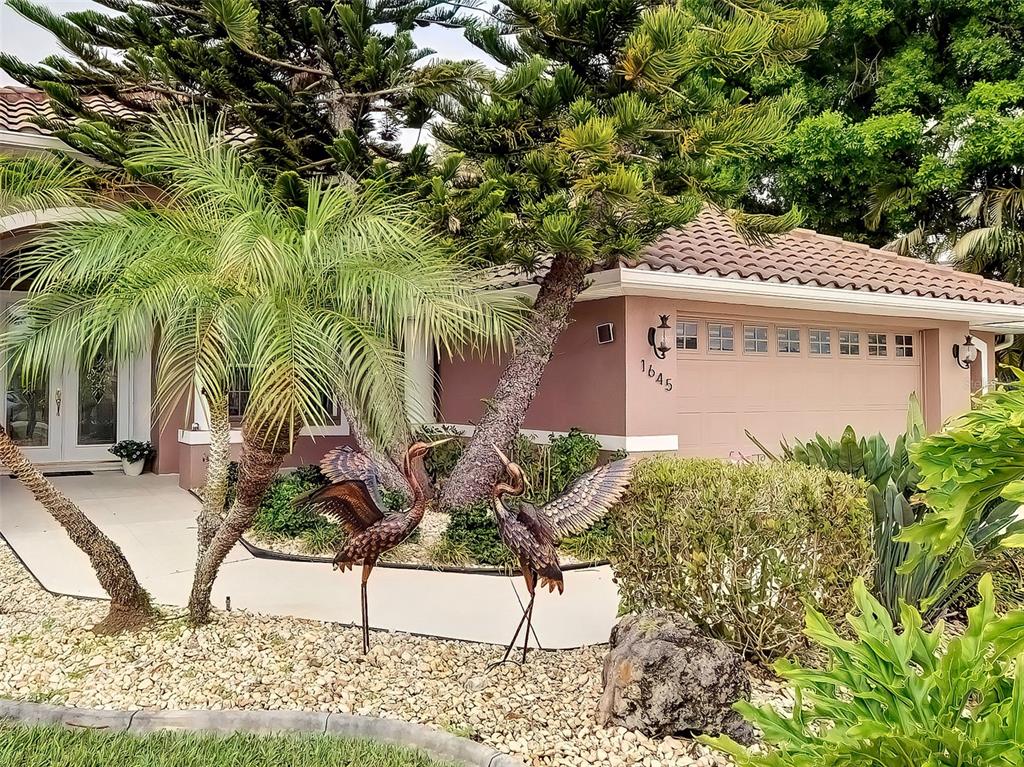 A pink house exterior features a garage, a palm tree, and two metal crane sculptures — 1645 PALMETTO PALM WAY, NORTH PORT, FL