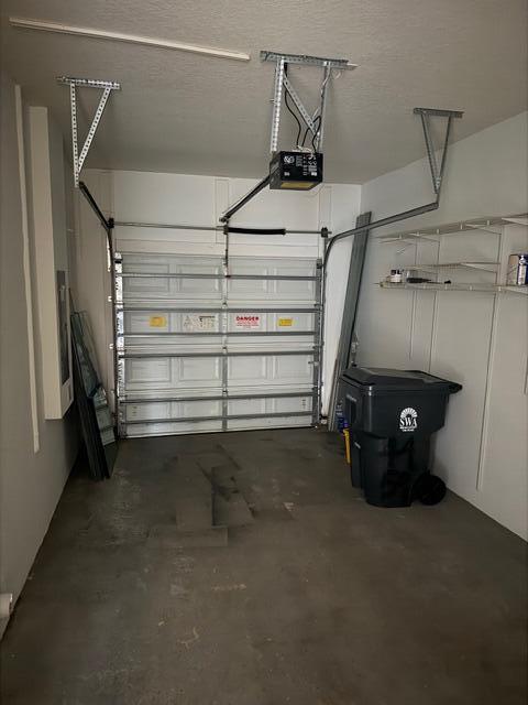 A single-car garage with a white sectional door, concrete floor, and overhead storage shelving — 4459 Cotswold Hills Drive, FL 33461, FL