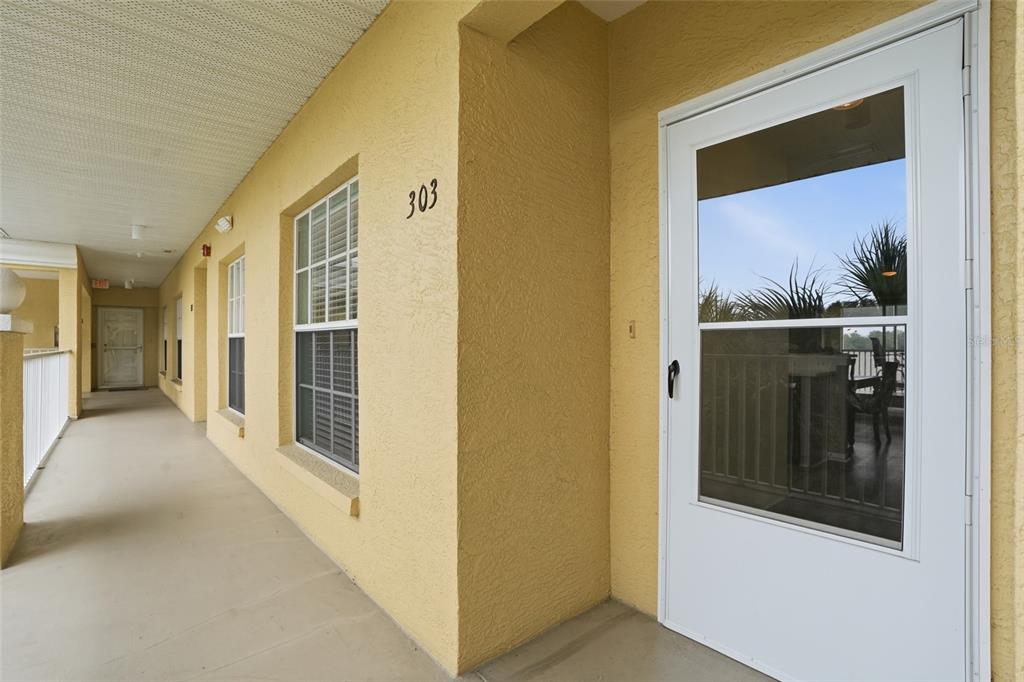 A view of a yellow exterior hallway with a numbered door and windows — 19355 WATER OAK DRIVE UNIT 303, PORT CHARLOTTE, FL