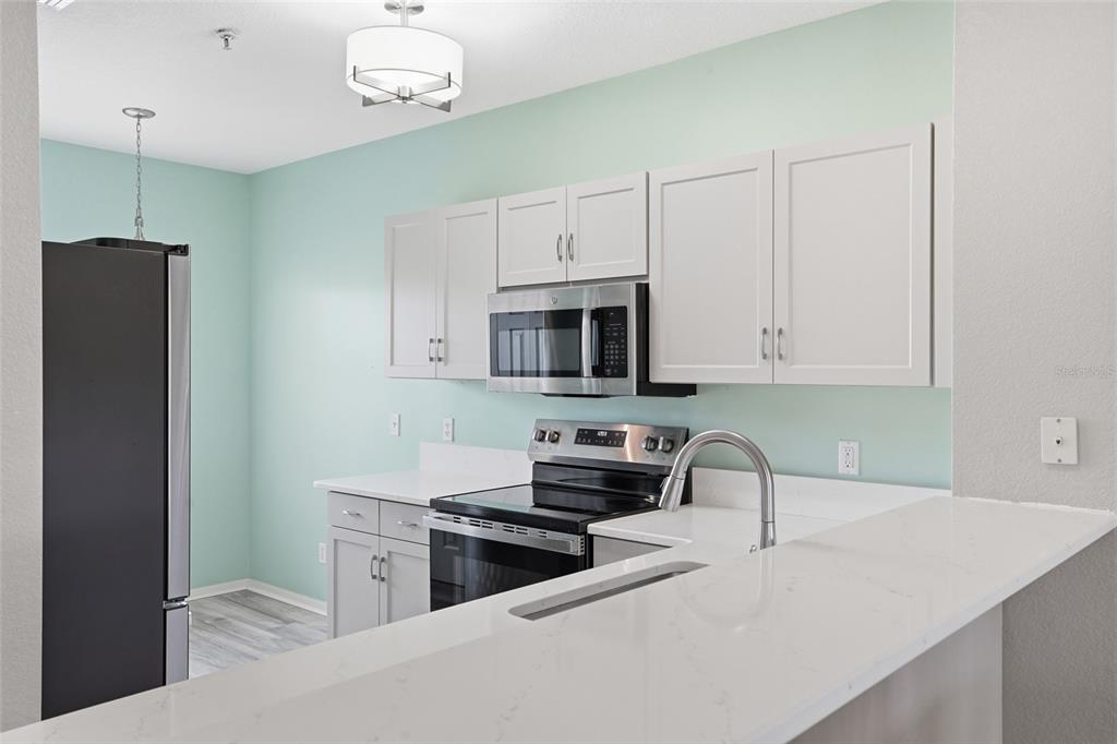 A kitchen features white cabinets, stainless steel appliances, and a white quartz breakfast bar — 19355 WATER OAK DRIVE UNIT 303, PORT CHARLOTTE, FL