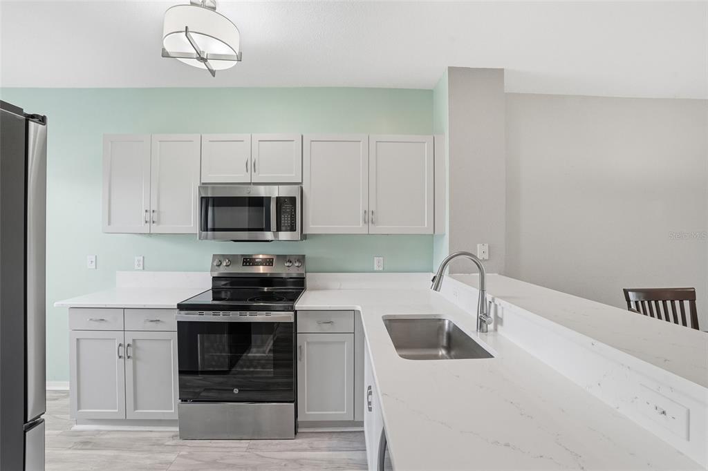 A kitchen features light gray cabinets, white countertops, stainless steel appliances, and light green walls — 19355 WATER OAK DRIVE UNIT 303, PORT CHARLOTTE, FL