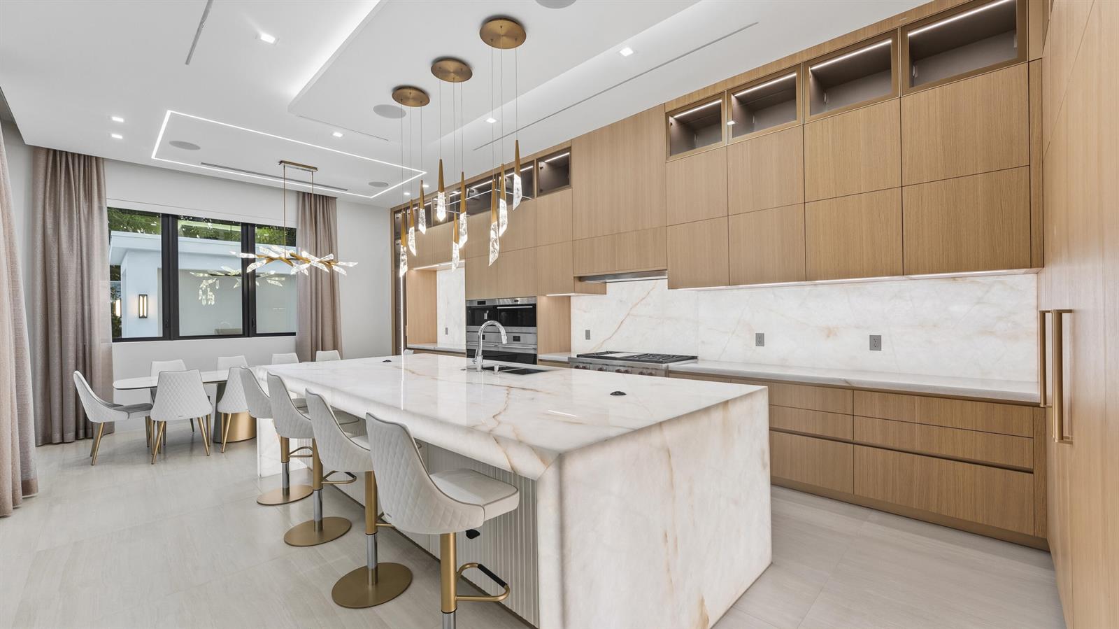 A modern kitchen features a large marble island, light wood cabinetry, and gold pendant lighting — 274 NE 3rd Court, Boca Raton FL 33432, BOCA RATON, FL
