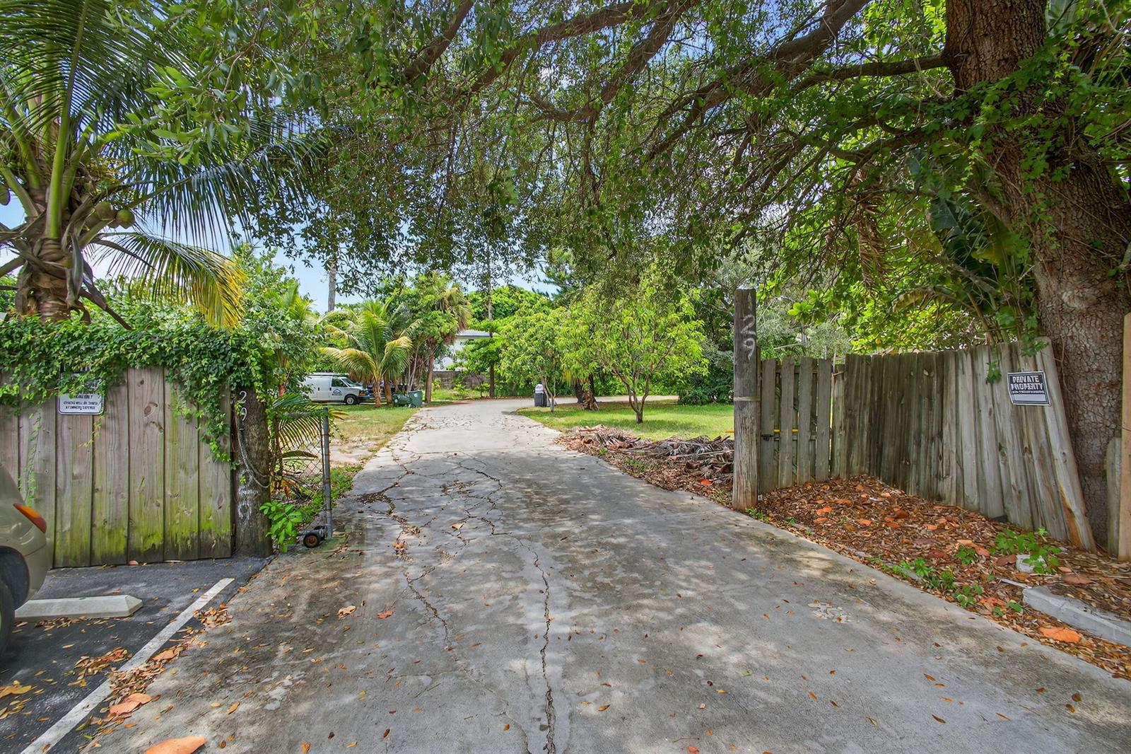 A concrete driveway leads through a wooden gate toward a tree-lined residential property — 129 Fleming Avenue, FL 33463, FL
