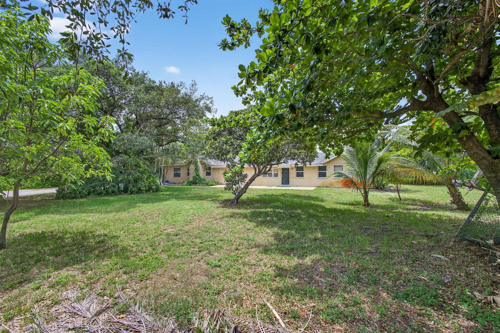 A single-story house with a light-colored exterior sits behind a large, grassy yard with trees — 129 Fleming Avenue, FL 33463, FL