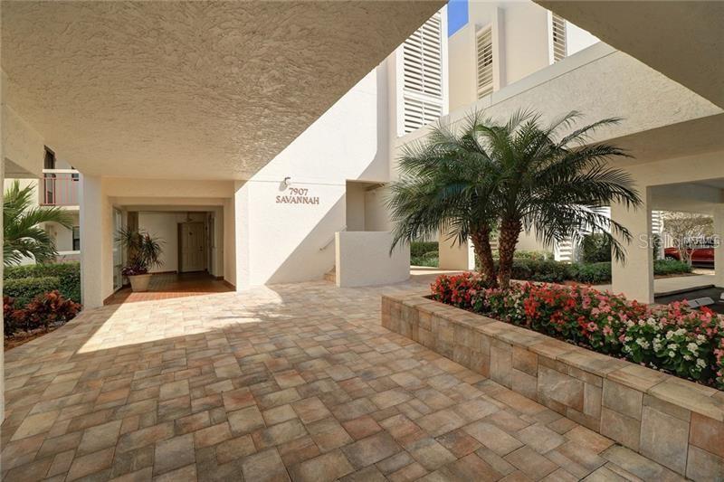 A paved outdoor entryway features a palm tree, a stone planter, and a building entrance — 7907 SAILBOAT KEY BOULEVARD S UNIT 105, SOUTH PASADENA, FL