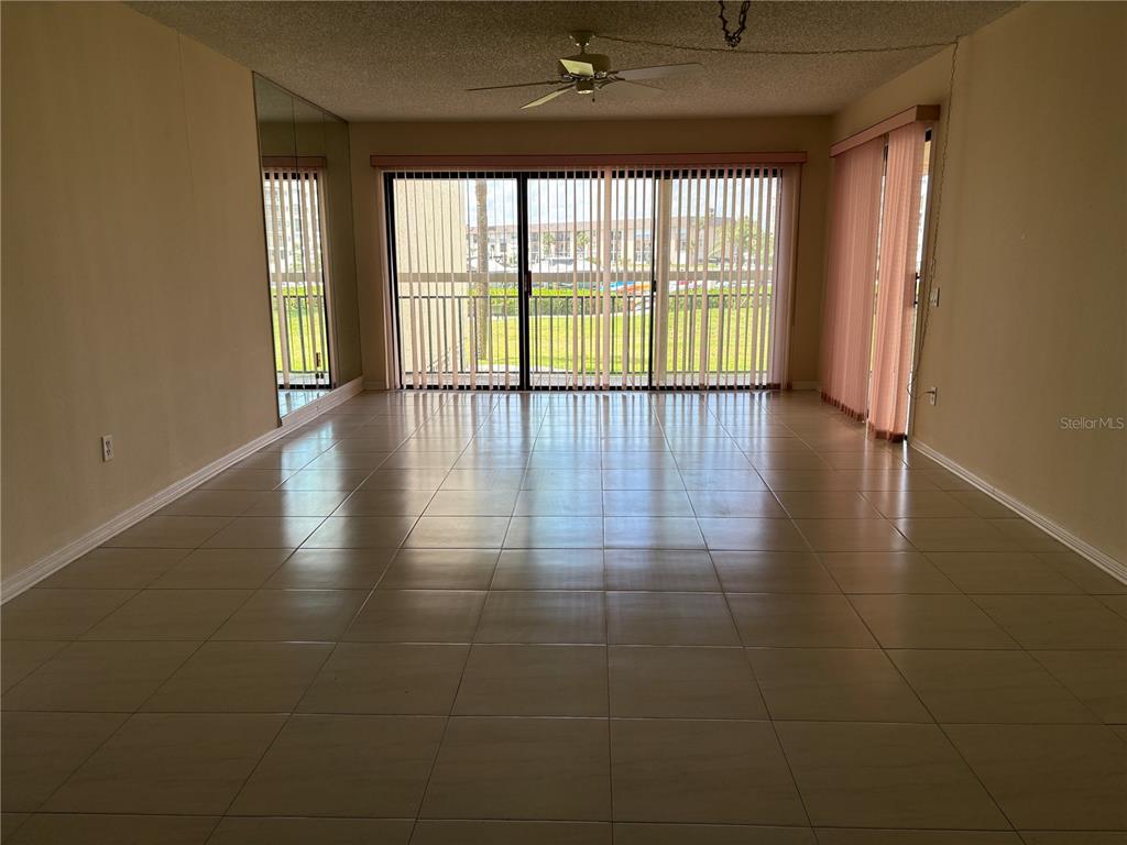 A spacious room features light-colored floor tiles, a ceiling fan, and large sliding glass doors — 7907 SAILBOAT KEY BOULEVARD S UNIT 105, SOUTH PASADENA, FL