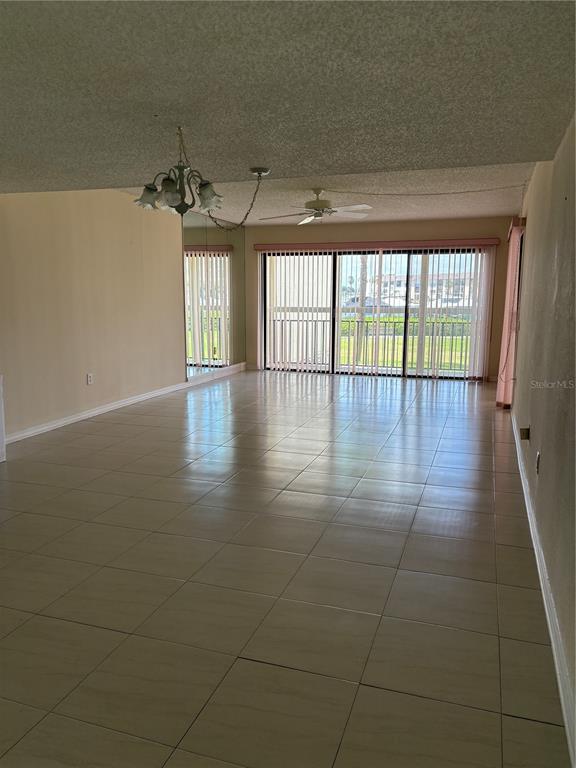 A spacious living area features light-colored floor tiles, a ceiling fan, and sliding glass doors — 7907 SAILBOAT KEY BOULEVARD S UNIT 105, SOUTH PASADENA, FL