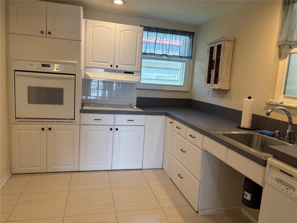A kitchen features white cabinets, a wall oven, a dark countertop, and a stainless sink — 7907 SAILBOAT KEY BOULEVARD S UNIT 105, SOUTH PASADENA, FL