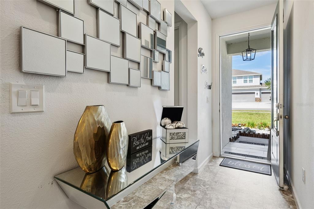 An entryway features a mirrored console table, wall art, and an open door to the outside — 31736 BROADWATER AVENUE, LEESBURG, FL