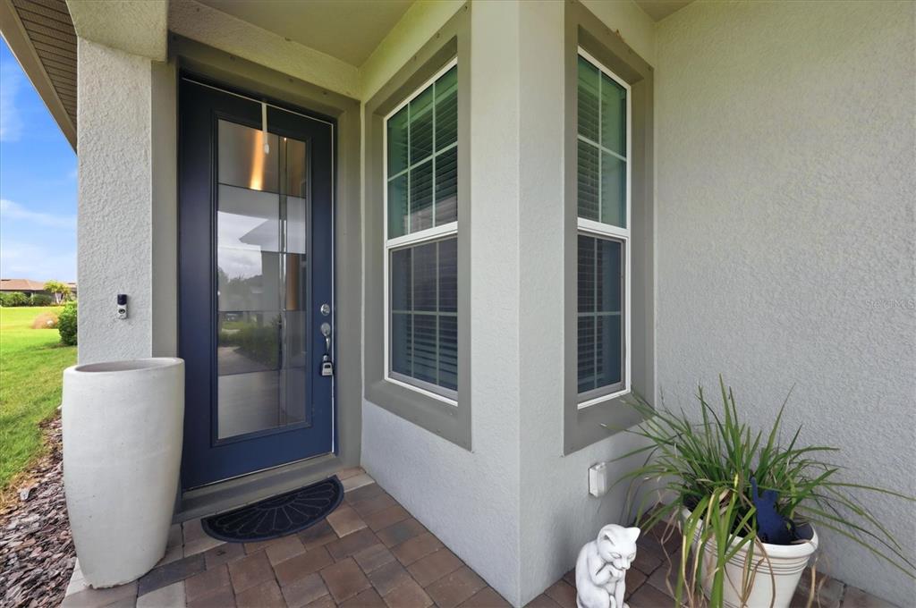 A dark blue front door with a glass panel sits beside two windows on a porch — 8706 OCEAN TIDES COVE, PARRISH, FL