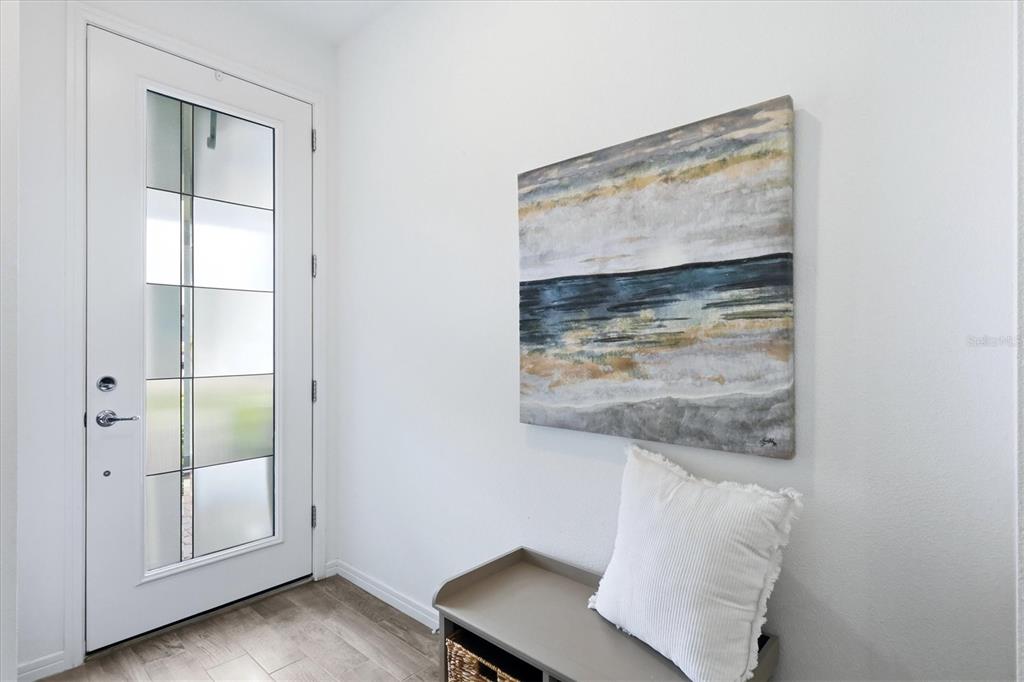 An entryway features a white door with glass panels, a bench, and abstract wall art — 8706 OCEAN TIDES COVE, PARRISH, FL