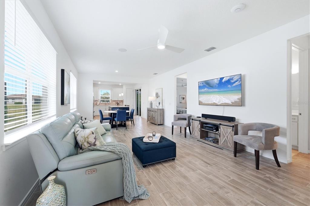 A bright, open-concept living room features light tile floors, a blue sofa, and a television — 8706 OCEAN TIDES COVE, PARRISH, FL