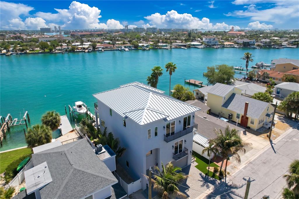An aerial view shows a multi-story house with a metal roof beside a waterway — 306 BAY PLZ, TREASURE ISLAND, FL