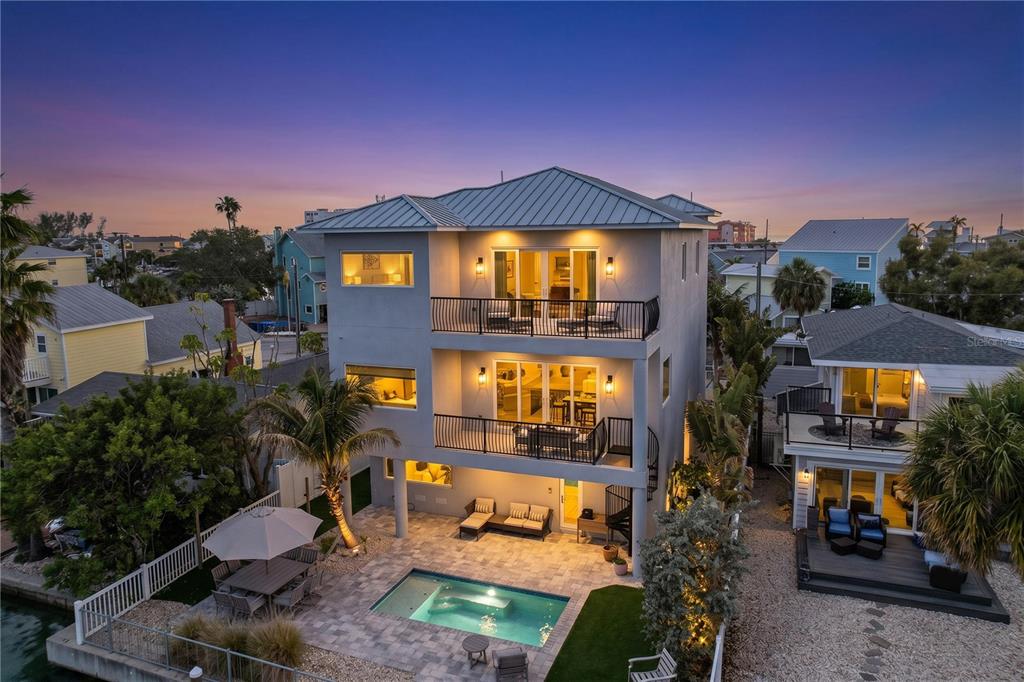 An aerial view of a three-story coastal home with balconies, a pool, and patio furniture — 306 BAY PLZ, TREASURE ISLAND, FL