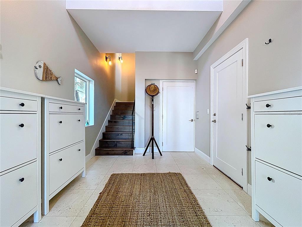 An entryway features tile flooring, white storage cabinets, a wooden staircase, and a coat rack — 306 BAY PLZ, TREASURE ISLAND, FL