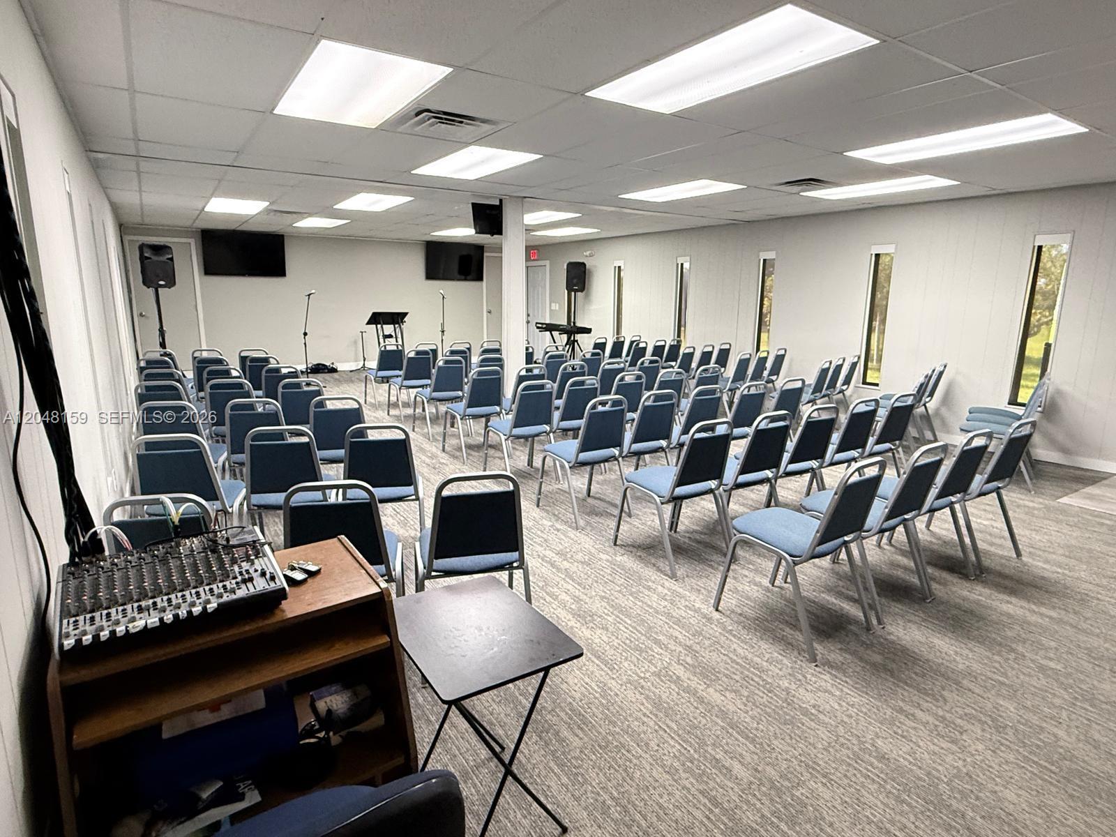 A meeting room features rows of blue chairs, a sound mixer, and a small stage — 18500 Griffin Rd, Southwest Ranches FL 33332, SOUTHWEST RANCHES, FL
