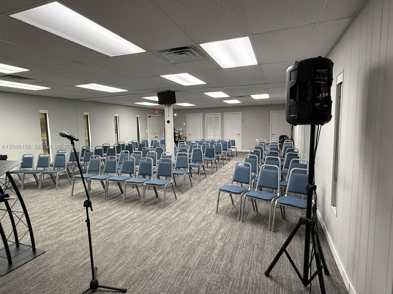 A meeting room features rows of blue chairs, a microphone stand, and a speaker — 18500 Griffin Rd, Southwest Ranches FL 33332, SOUTHWEST RANCHES, FL