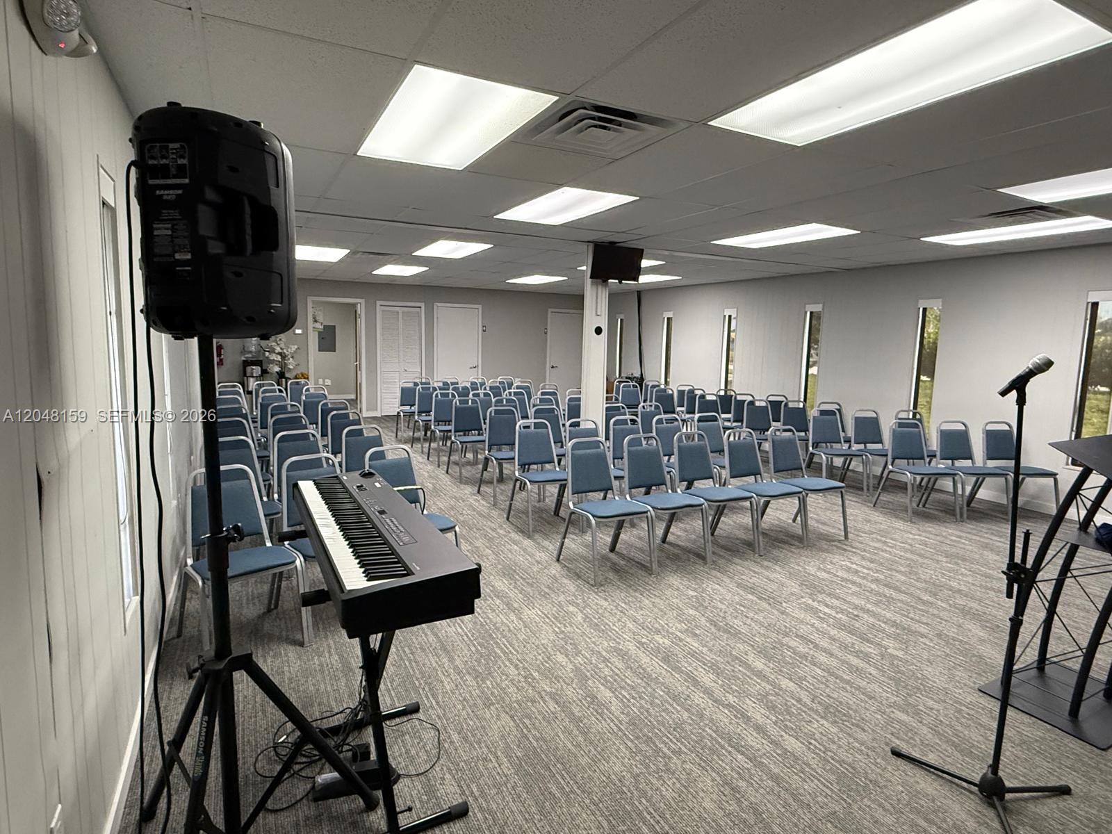 A meeting room features rows of blue chairs, a keyboard on a stand, and a speaker — 18500 Griffin Rd, Southwest Ranches FL 33332, SOUTHWEST RANCHES, FL