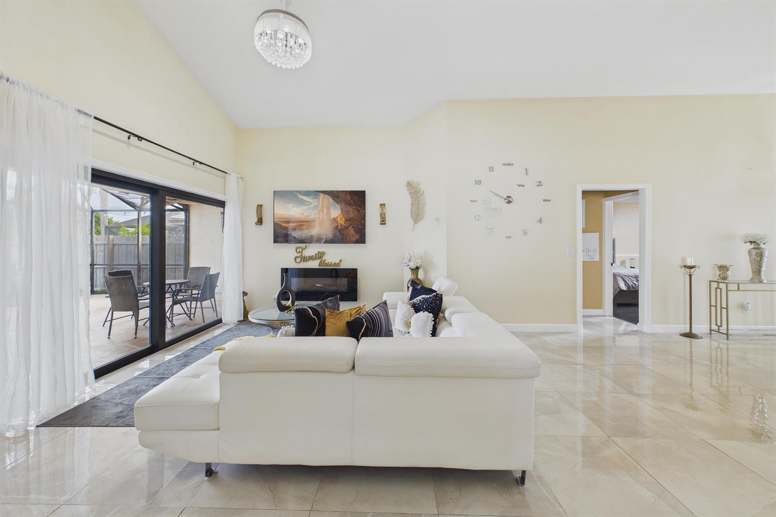 A bright living room features a white sectional sofa, fireplace, wall clock, and sliding glass doors — 169 Executive Circle, Boynton Beach FL 33436, BOYNTON BEACH, FL