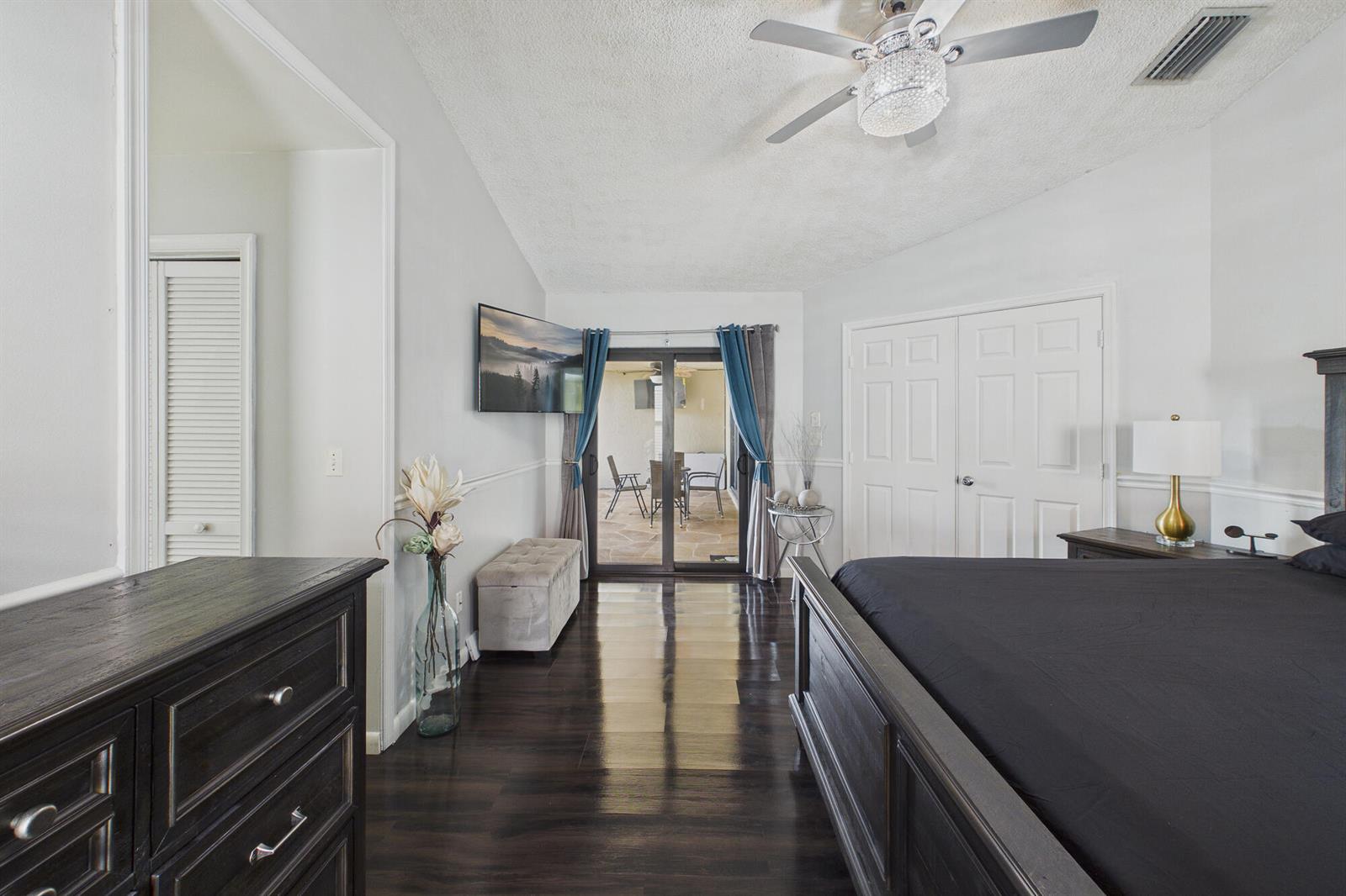 A bedroom features dark wood flooring, a black bed frame, and sliding glass doors — 169 Executive Circle, Boynton Beach FL 33436, BOYNTON BEACH, FL