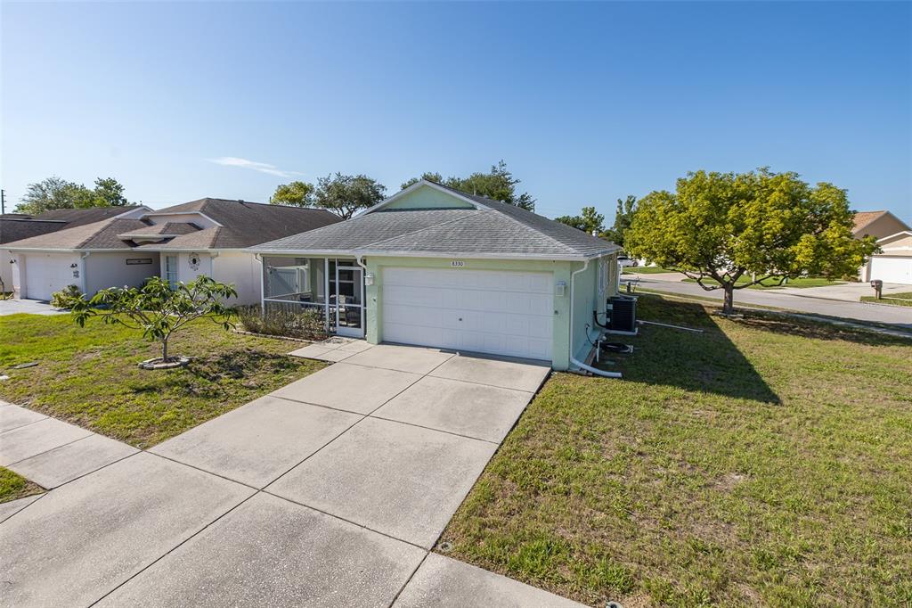 A light green house features a white garage door and a screened-in front porch — 8330 GOLDOME DRIVE, PORT RICHEY, FL