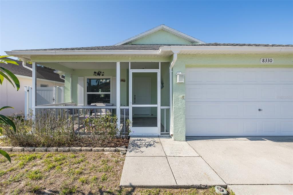 A light green single-story house with a two-car garage and a screened-in front porch — 8330 GOLDOME DRIVE, PORT RICHEY, FL
