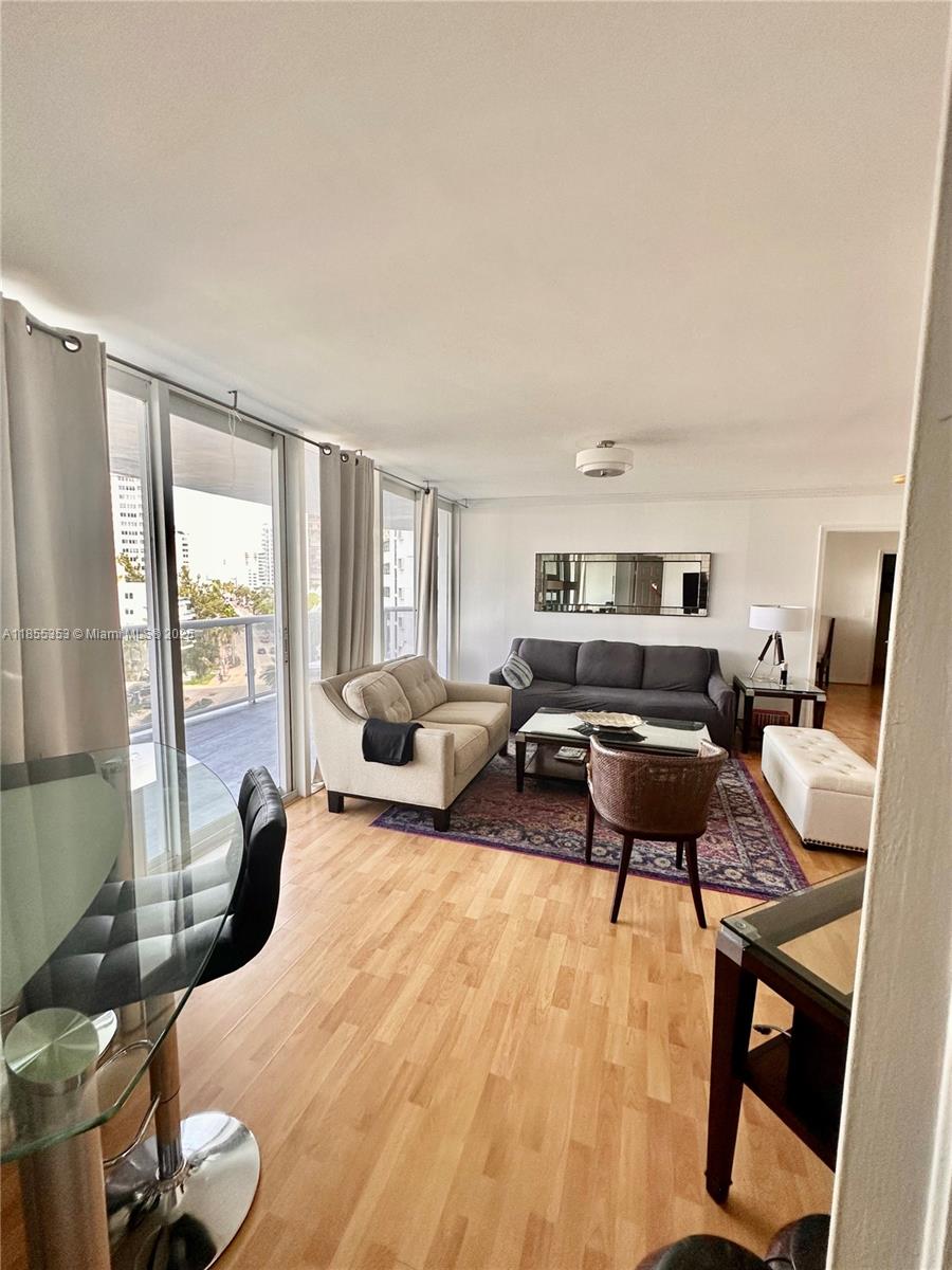 A living room features light wood flooring, a beige sofa, a dark gray sofa, and a balcony — 6301 Collins Ave # 806, Miami Beach FL 33141, MIAMI BEACH, FL