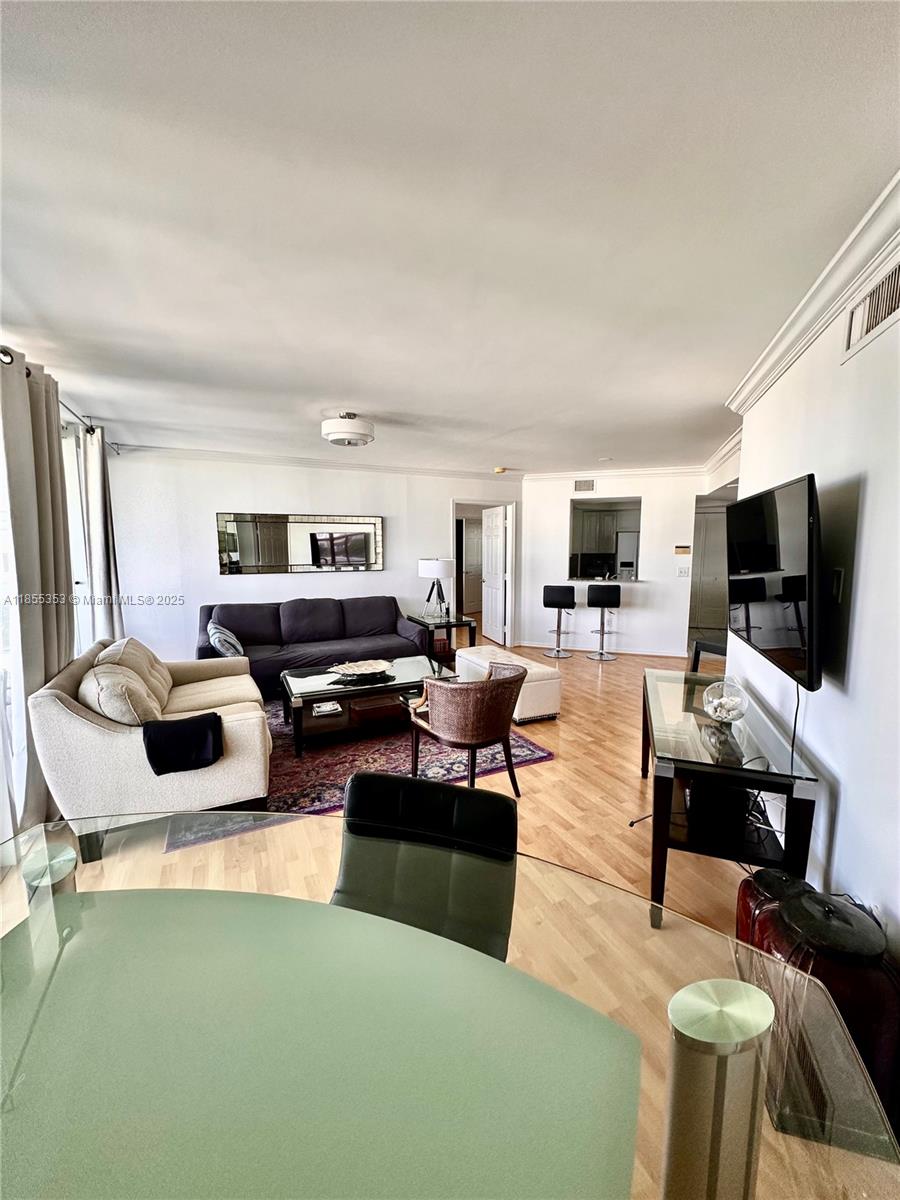 A living room features light wood flooring, a dark sofa, and a glass-topped dining table — 6301 Collins Ave # 806, Miami Beach FL 33141, MIAMI BEACH, FL