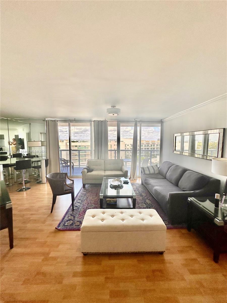 A living room with hardwood floors, a gray sofa, a beige ottoman, and balcony access — 6301 Collins Ave # 806, Miami Beach FL 33141, MIAMI BEACH, FL