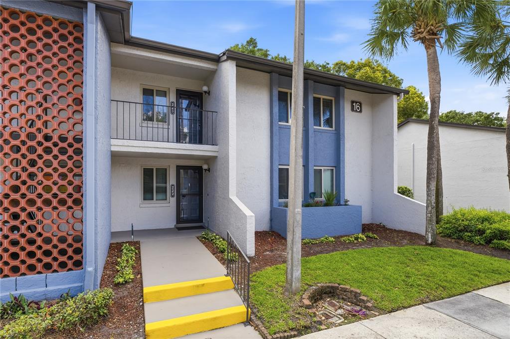 A two-story apartment building exterior features a decorative breeze block wall and yellow-painted steps — 16 ESCONDIDO CIRCLE UNIT 223, ALTAMONTE SPRINGS, FL