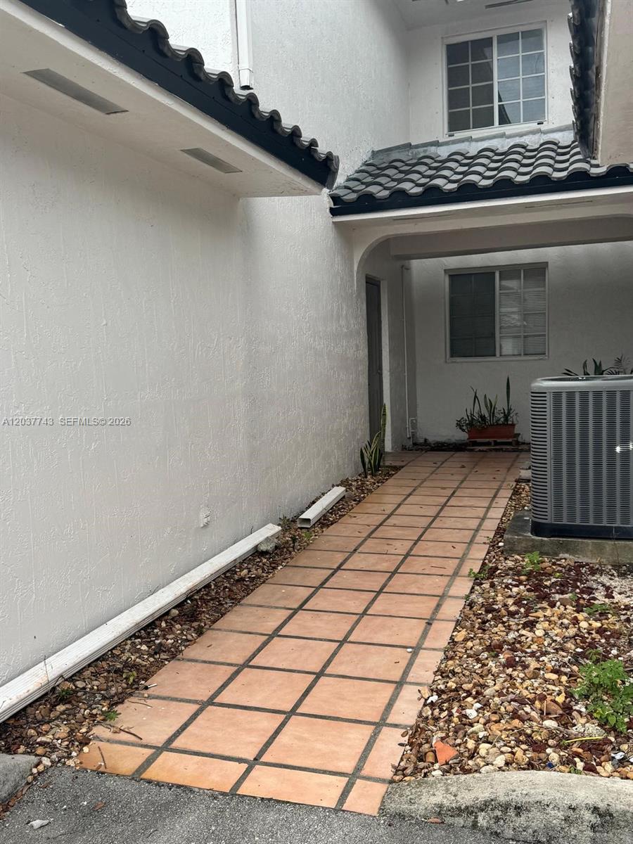 A tiled walkway leads to a doorway beneath a covered exterior passage next to an AC unit — 7502 NW 175th St # 7502, Hialeah FL 33015, HIALEAH, FL