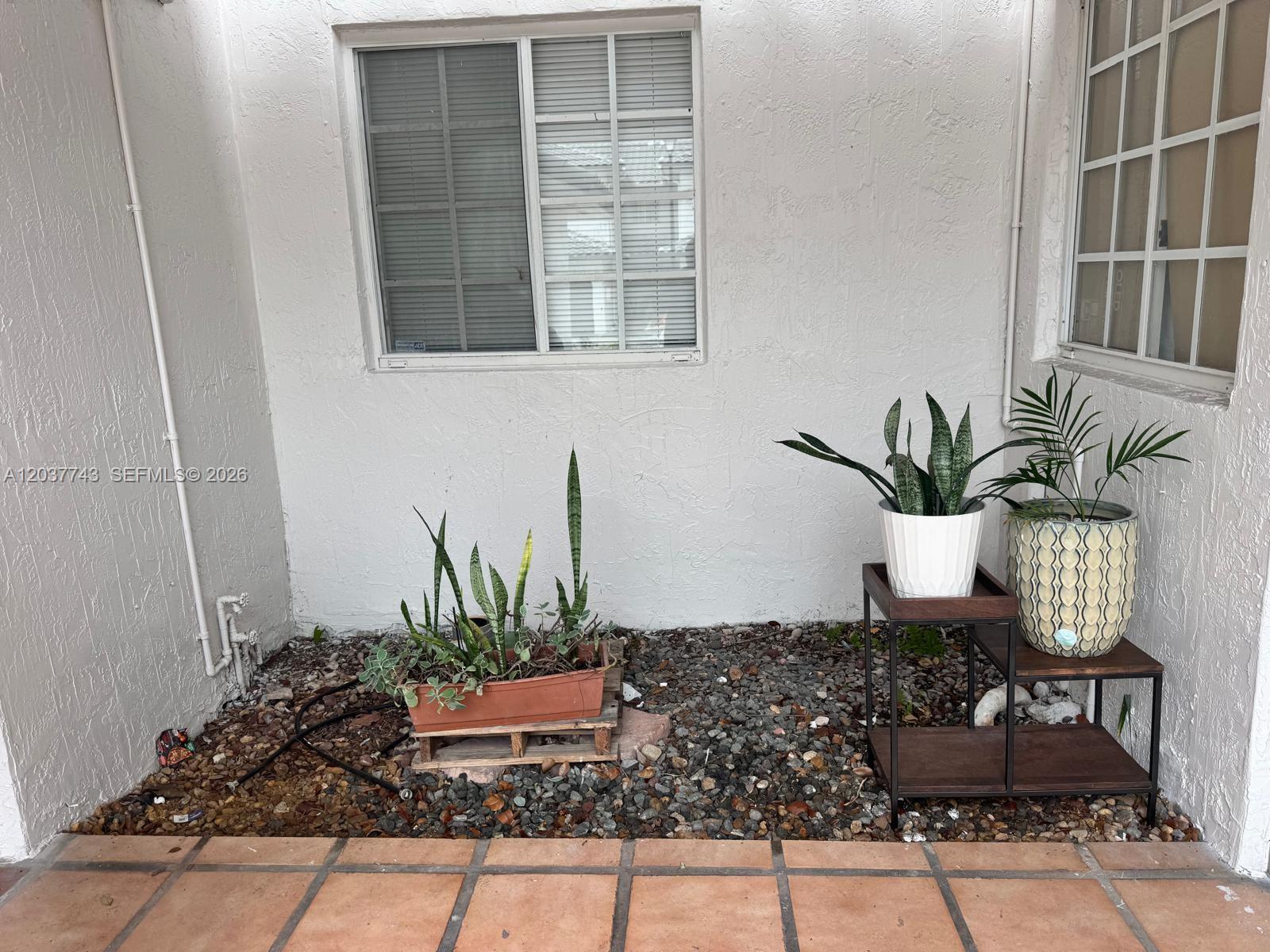 A patio area features a gravel ground, potted plants, and a small wooden plant stand — 7502 NW 175th St # 7502, Hialeah FL 33015, HIALEAH, FL