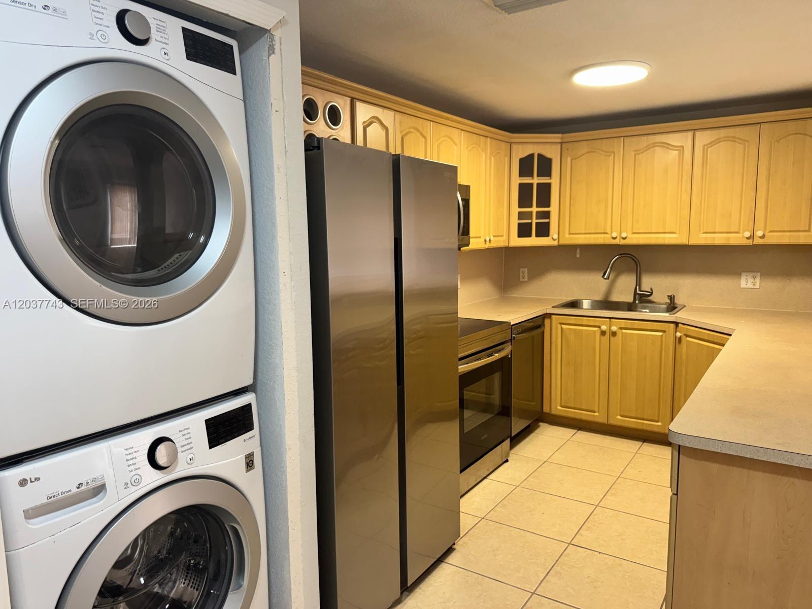 A kitchen features light wood cabinets, stainless steel appliances, and a stacked washer-dryer unit — 7502 NW 175th St # 7502, Hialeah FL 33015, HIALEAH, FL