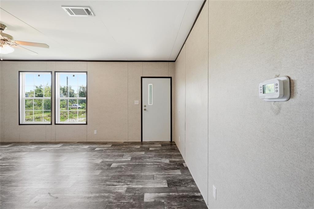 A living room with light-colored walls, wood-look flooring, a ceiling fan, and a white door — 17381 NW 262ND STREET, OKEECHOBEE, FL