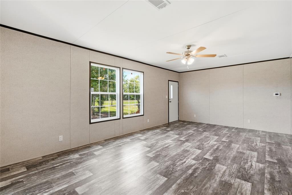 A living room features light-colored paneled walls, wood-look flooring, two windows, and a ceiling fan — 17381 NW 262ND STREET, OKEECHOBEE, FL