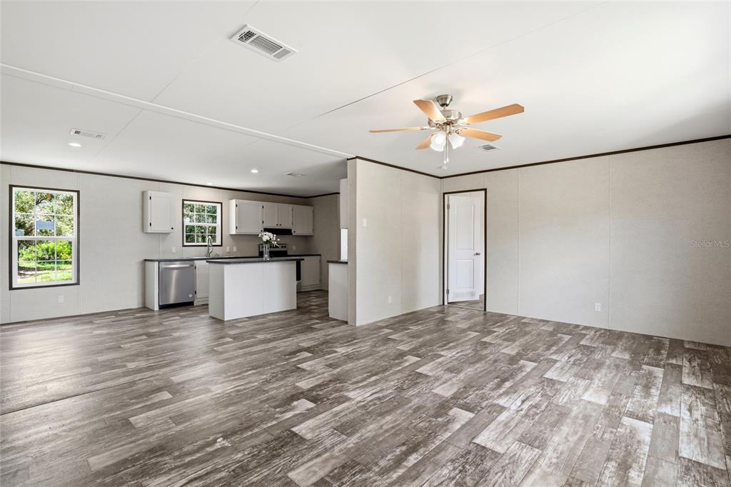 An open-concept living area features wood-look flooring, a ceiling fan, and an adjacent kitchen — 17381 NW 262ND STREET, OKEECHOBEE, FL