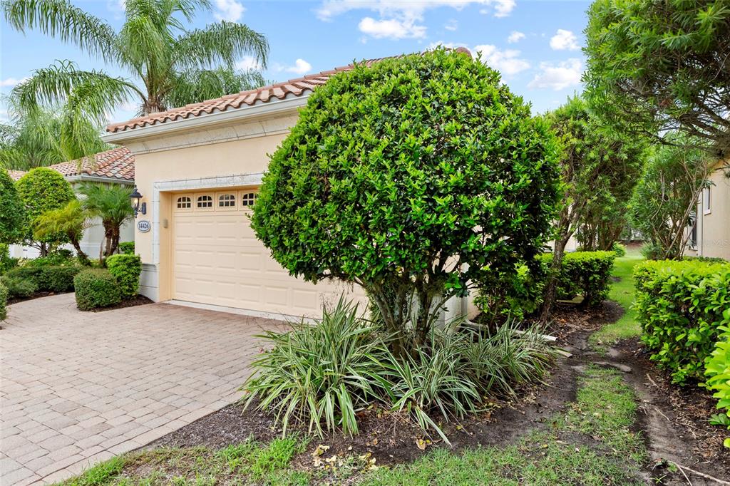 A beige house exterior features a two-car garage, a paved driveway, and manicured landscaping — 14426 WHITEMOSS TERRACE, LAKEWOOD RANCH, FL