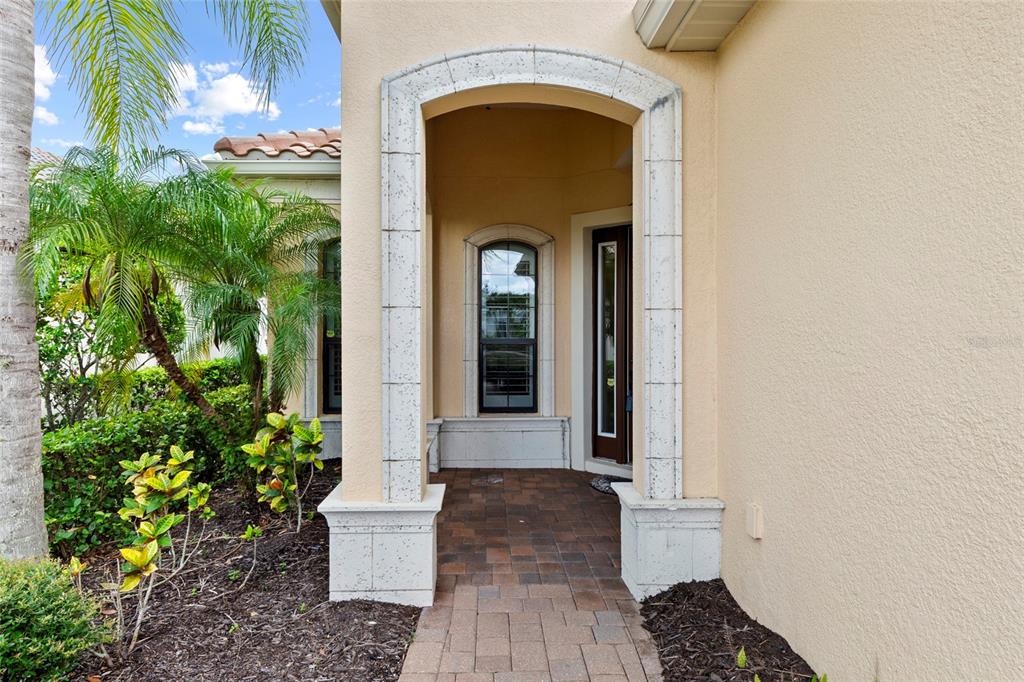 A stone-arched entryway leads to a front door and window on a stucco house exterior — 14426 WHITEMOSS TERRACE, LAKEWOOD RANCH, FL