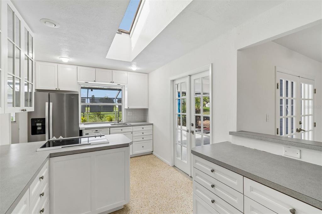 A white kitchen features gray countertops, stainless steel appliances, a skylight, and glass-paned doors — 830 LA JOLLA AVENUE, SUN CITY CENTER, FL