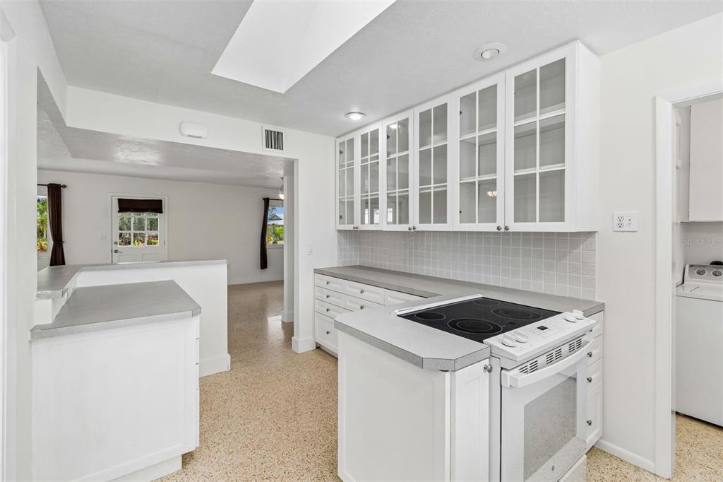 A white kitchen features glass-front cabinets, a glass-top stove, and light-colored countertops — 830 LA JOLLA AVENUE, SUN CITY CENTER, FL