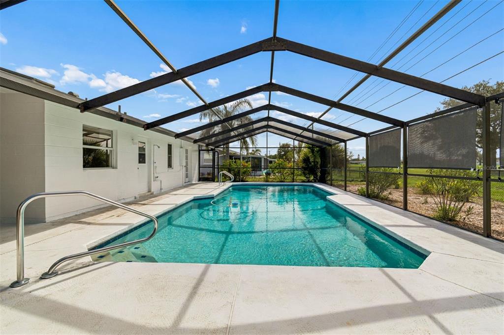 A swimming pool with a metal-framed screen enclosure sits on a concrete patio — 830 LA JOLLA AVENUE, SUN CITY CENTER, FL