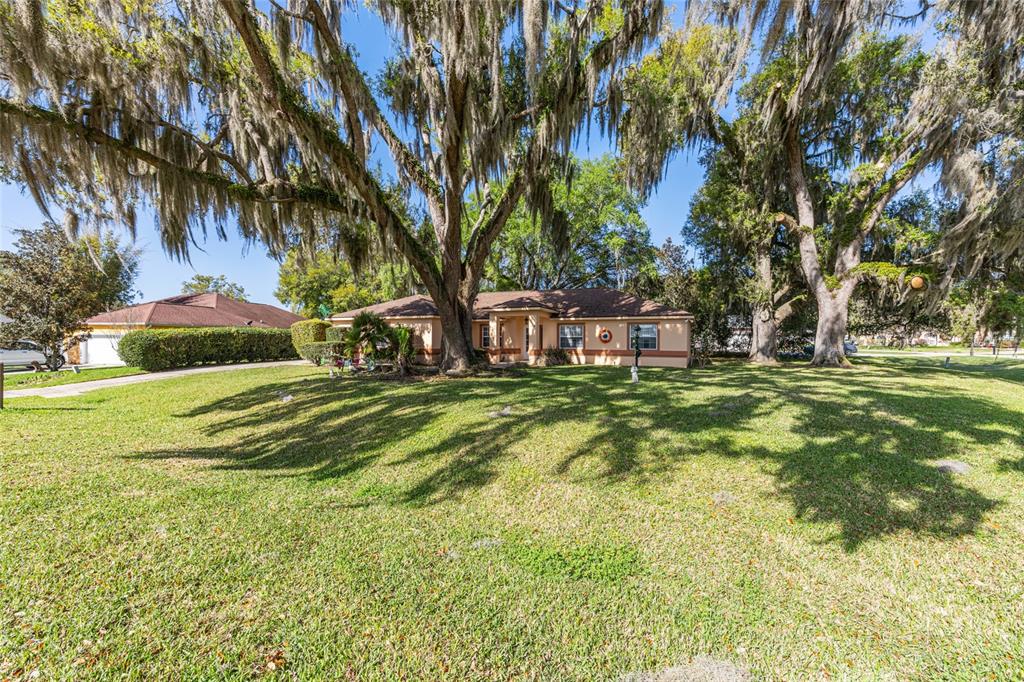 A single-story house with a tan exterior stands behind a large lawn with mature trees — 10090 SW 78TH COURT, OCALA, FL