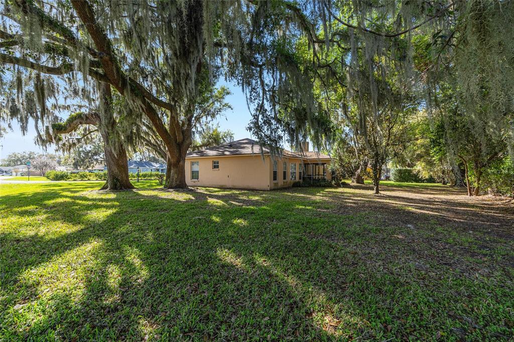 A tan house sits on a grassy lot shaded by large, moss-covered oak trees — 10090 SW 78TH COURT, OCALA, FL