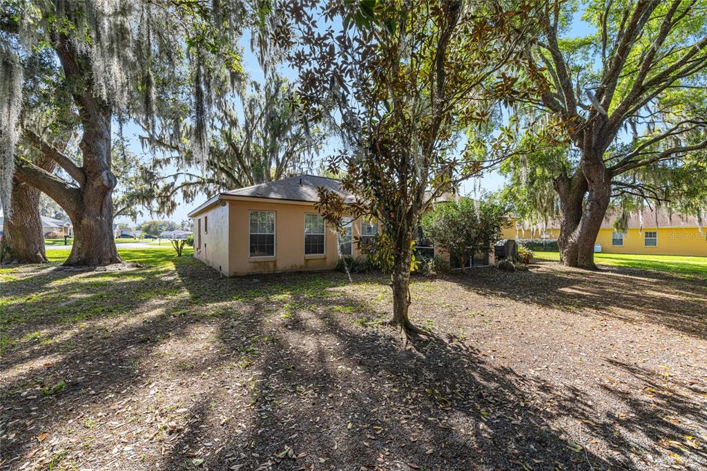 The exterior of a tan house is surrounded by large trees with hanging Spanish moss — 10090 SW 78TH COURT, OCALA, FL