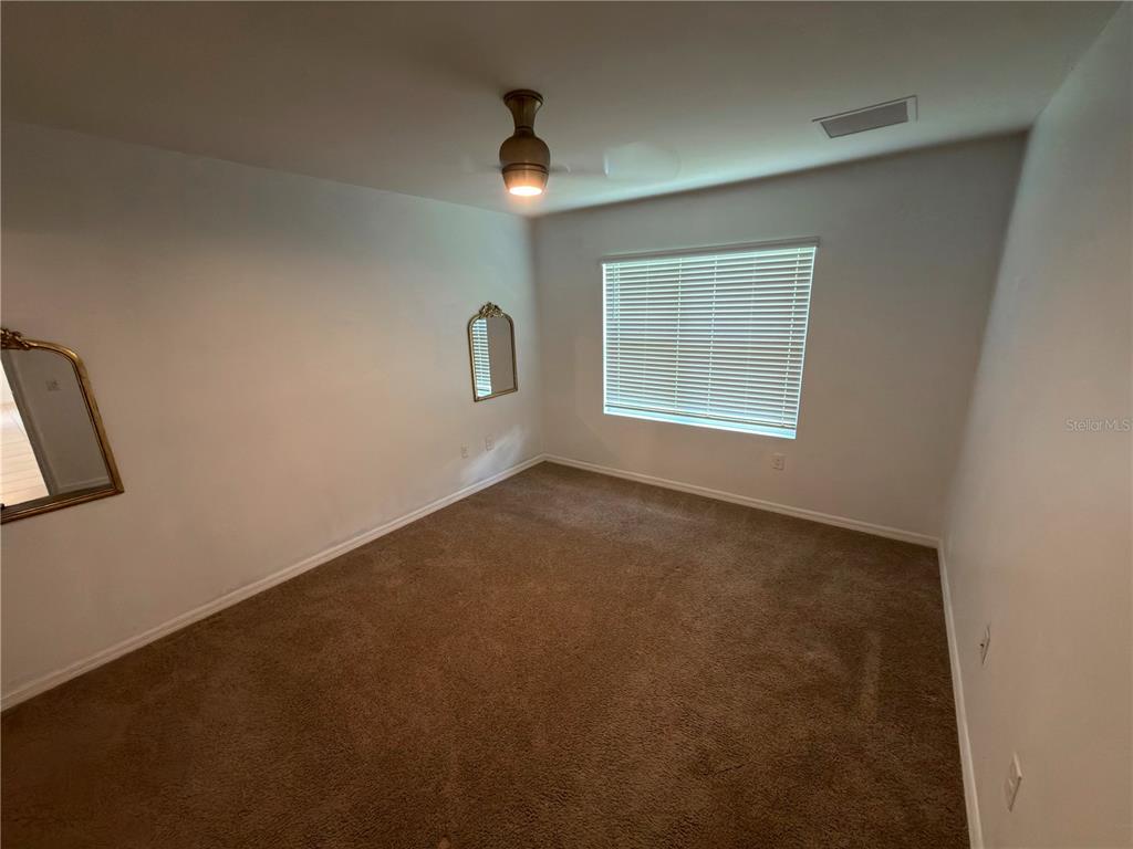 An empty bedroom features brown carpet, white walls, a ceiling fan, and two wall mirrors — 27956 ARROWHEAD CIRCLE, PUNTA GORDA, FL