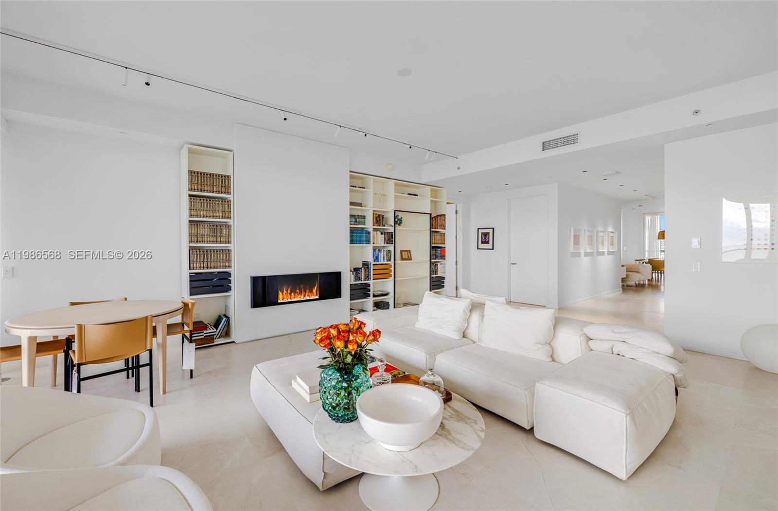 A bright living room features a fireplace, built-in bookshelves, white furniture, and a dining area — 9705 Collins Ave # 802N, Bal Harbour FL 33154, BAL HARBOUR, FL