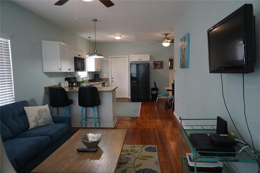 An open-concept living room and kitchen featuring hardwood floors, a blue sofa, and black appliances — 601 N OSCEOLA AVENUE, CLEARWATER, FL